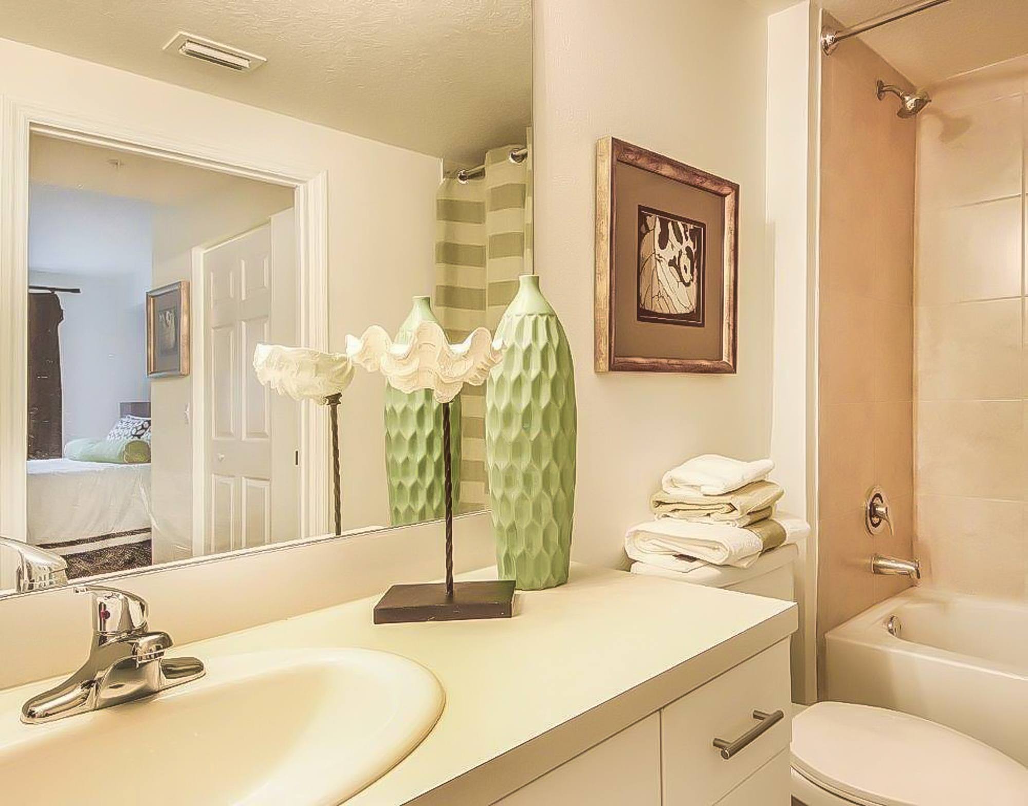 A bathroom with a white sink and a green vase.